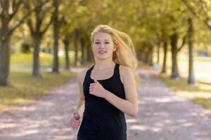 joven mujer rubia corriendo en un camino con grandes árboles foto