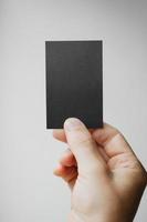 Mano que sostiene la tarjeta de visita vertical negra en el gris borroso foto