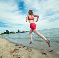Young lady running at the sunny summer sand beach. Workout photo