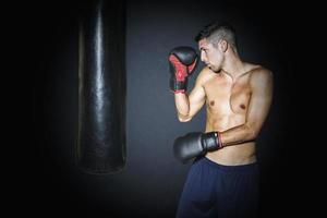 hombre musculoso entrenando con saco de boxeo en el gimnasio foto