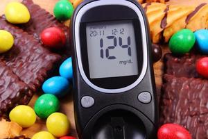 Glucose meter with heap of sweets, diabetes and unhealthy food photo