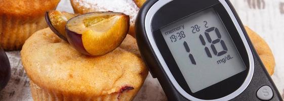 Glucometer and muffins with plums on wooden background, diabetes