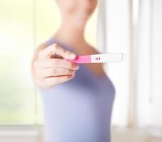 Woman wearing purple best holding up positive pregnancy test photo