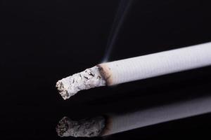 lit single cigarette with smoke  on black background photo