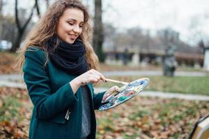 Young woman drawing in easel on the park background