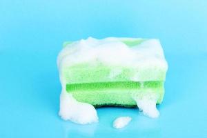 Sponge with foam of dishwashing liquid on blue background photo