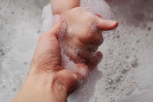 mother holds the hand in a bathtub with foam
