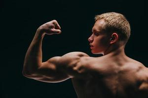 muscular young man showing his biceps isolated on black background photo
