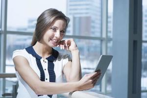 Pensive businesswoman smiling at camera holding digital tablet photo