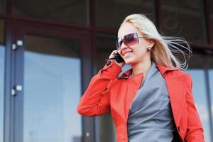 mujer joven llamando por teléfono contra las ventanas de la oficina