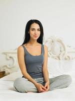Young woman sitting cross legged on bed, portrait photo