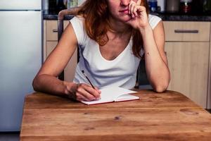 Bored woman writing in her kitchen photo
