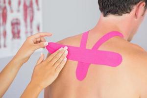 Physiotherapist putting pink kinesio tape on male patients back