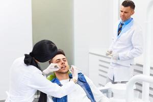 Dentista con asistente examinar los dientes en la silla de dentistas.