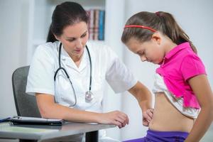 Doctor checking stomach of sick girl photo
