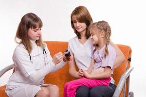 Pediatrician is going to give sick child sitting mother medicine photo