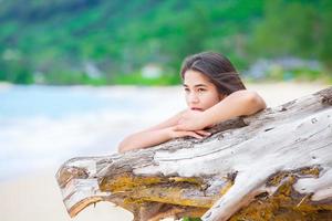 Hermosa jovencita en la playa rezando por el registro de madera flotante