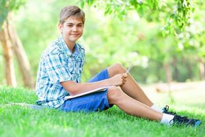 Muchacho adolescente con libros y cuaderno en el parque.