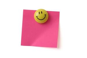 Un imán amarillo de cara sonriente sosteniendo un papel adhesivo rosa