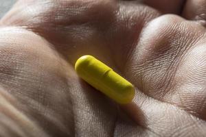 Bare hand holding one yellow medicinal tablet photo
