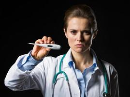 Doctor serio mujer mostrando termómetro aislado en negro