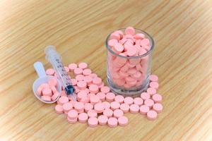 pastillas de color rosa y una jeringa en la mesa por concepto de atención médica
