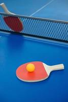 raquetas de ping-pong y pelota sobre una mesa de ping-pong azul