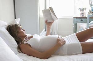 mujer embarazada leyendo un libro mientras está acostado en la cama foto