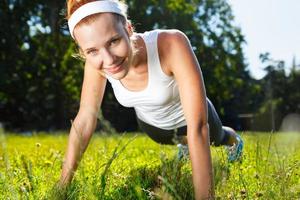 Young woman doing push ups on green grass.