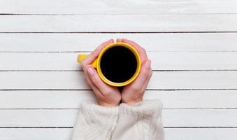 Female hands holding cup of coffee on wooden table. photo