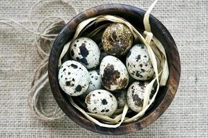Quail eggs in wooden bowl on sack background photo