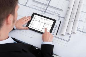 Architect Using Digital Tablet On Blueprint In Office photo