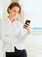 Young busineswoman standing with phone in office lobby