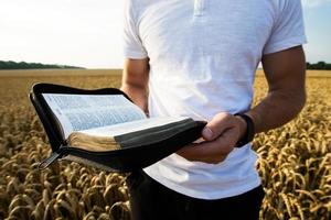 Man holding open Bible in a wheat field photo