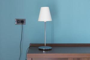 Lámpara con pantalla blanca sobre una mesa de madera con fondo azul. foto