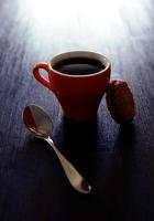 Orange mug with coffee, teaspoon and cookie on table photo