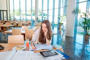 Chica estudiando en el comedor de la universidad con fresco y pastel foto