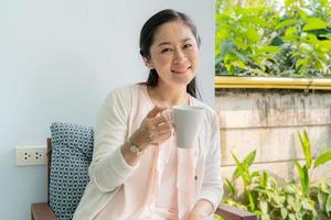 mujer asiática de mediana edad sentado y tomando café en el patio trasero. foto