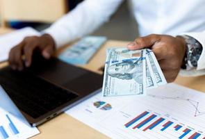 Empresario contando efectivo en mano con gráfico financiero en el escritorio foto