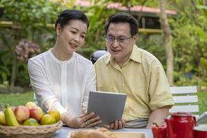 Elderly couple sits outdoors watching tablet screen photo