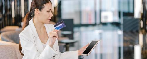 Una mujer asiática con tarjeta de crédito para compras en línea en el vestíbulo foto