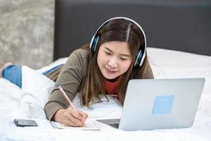 Young Asian woman using laptop and writing at home photo