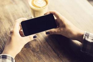 manos de la niña con teléfono inteligente y café en una mesa de madera foto