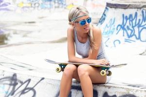 Young girl with skateboard sitting in skatepark photo