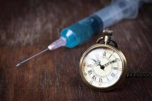 Health concept , old clock with syringe on wood table. photo
