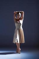 Joven bailarina hermosa en vestido beige bailando sobre fondo gris foto