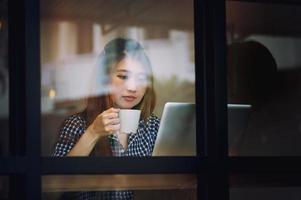 Asia mujer beber café y trabajar en la computadora portátil en la cafetería