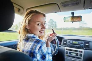 woman applying lipstick in a car while driving