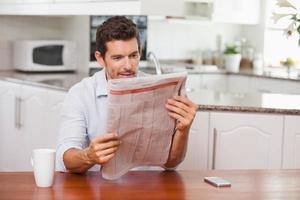Hombre concentrado leyendo el periódico en la cocina