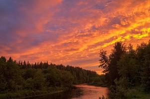 Bright dramatic sunset over river with forest along riverside